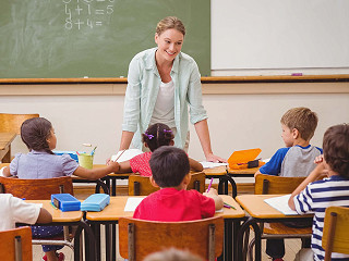 Ein Lehrer steht hinter dem Pult vor einer Grundschulklasse.